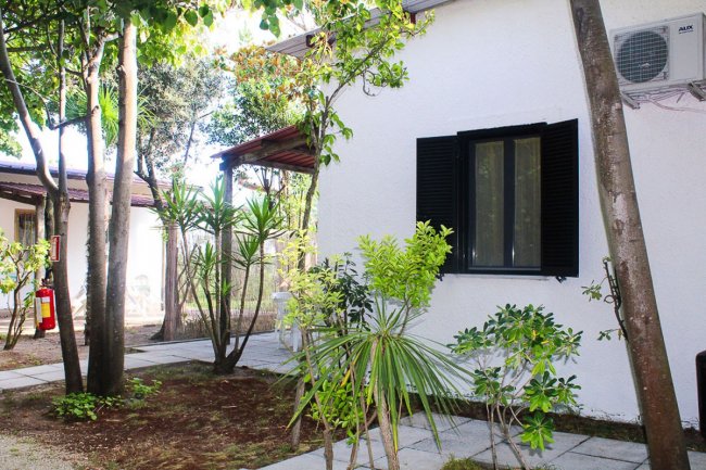 Casetta bianca con finestre nere in un giardino alberato.