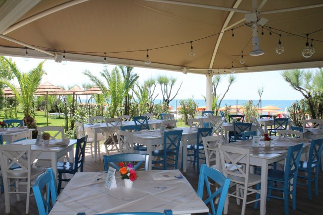 Sala da pranzo all'aperto con sedie bianche e blu, vista mare.