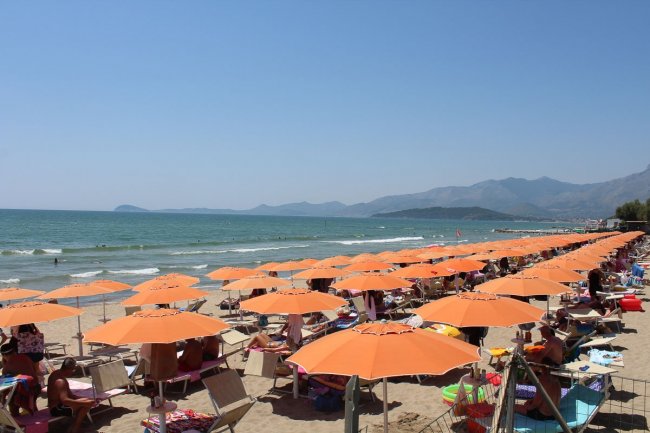 Spiaggia con ombrelloni arancioni e sdraio affollata di bagnanti.