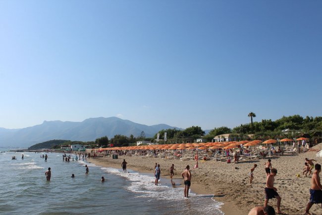 Bagnanti sulla riva di una spiaggia con montagne sullo sfondo.