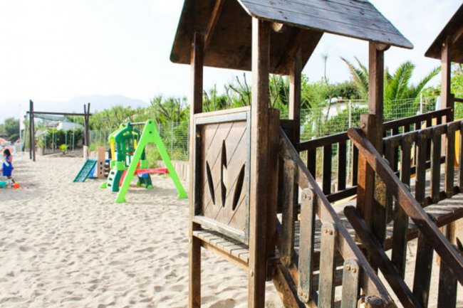 Parco giochi sulla sabbia con struttura in legno e scivolo colorato.
