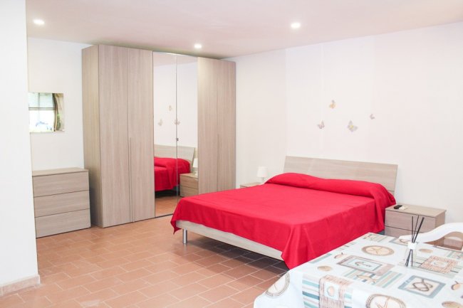 Una camera da letto con un letto matrimoniale rosso, armadio a specchi e comodino.