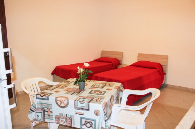 Stanza con due letti singoli coperti da coperte rosse e un tavolo con tovaglia geometrica.