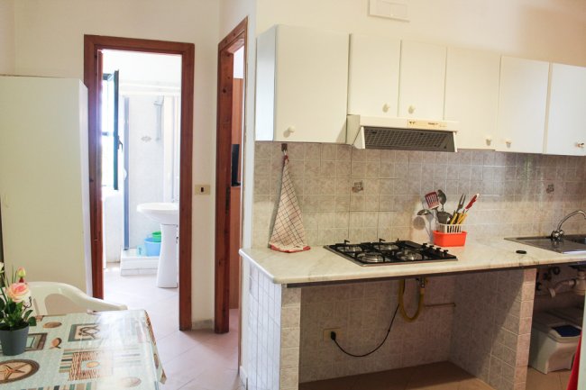 Cucina con piano cottura a gas, pareti con piastrelle bianche e vista di un bagno in fondo.