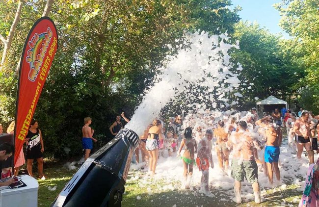 Festa all'aperto con persone coperte di schiuma sparata da un cannone.