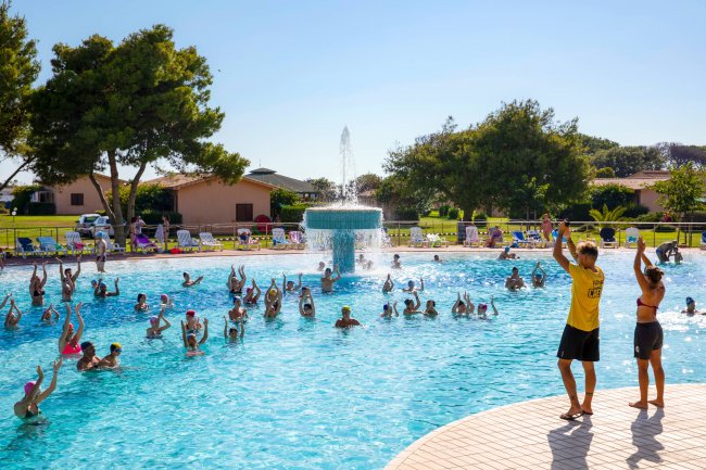 Persone in piscina seguono una lezione di acquagym, cielo sereno.