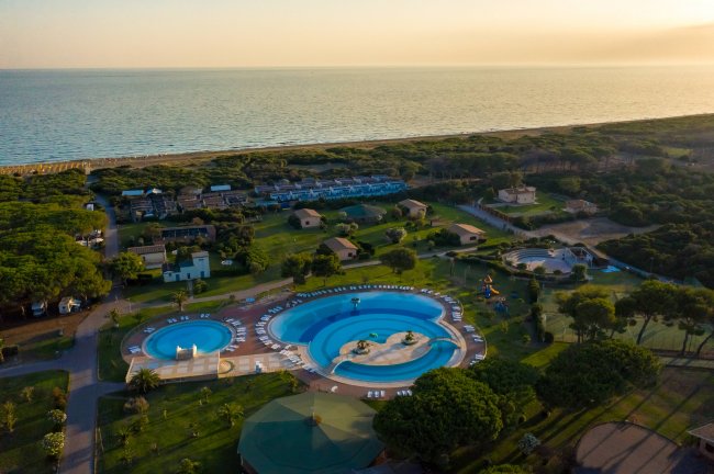 Complesso di piscine circondato da verde e vista sul mare al tramonto.