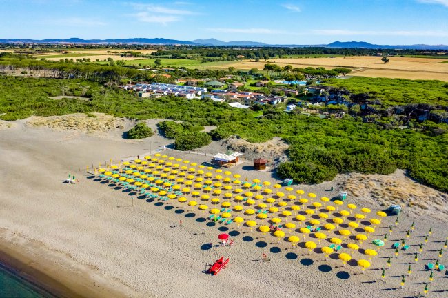 Spiaggia con ombrelloni gialli allineati e una torretta di salvataggio rossa.