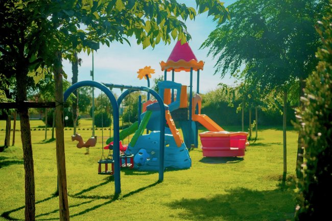 Parco giochi colorato con altalene e scivolo su prato verde.