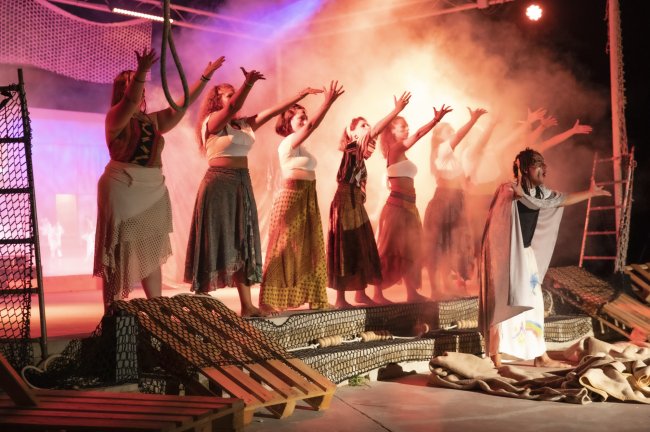 Persone sul palco che alzano le braccia in una performance teatrale.
