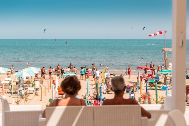 Due persone sedute osservano la spiaggia affollata.