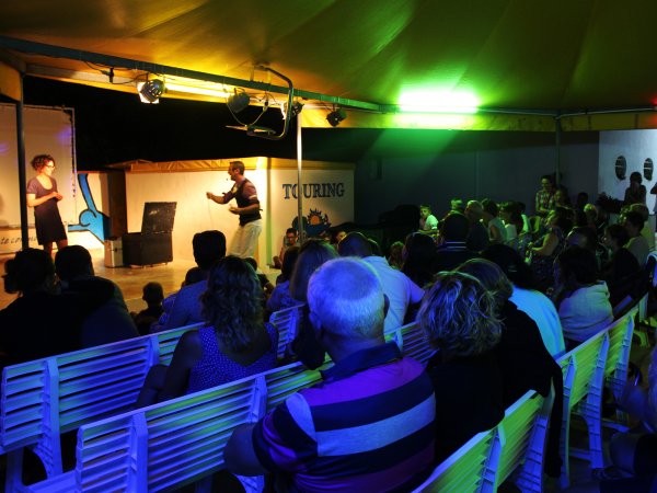 Una performance su un palco sotto una tenda con spettatori seduti.