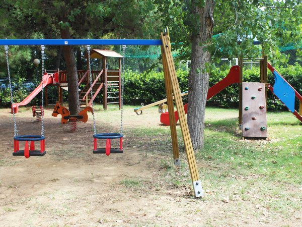 Parco giochi con altalene, scivolo e parete da arrampicata tra alberi.