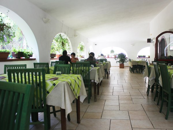 Una sala interna con tavoli coperti da tovaglie verde chiaro e sedie verdi, alcune persone sedute.