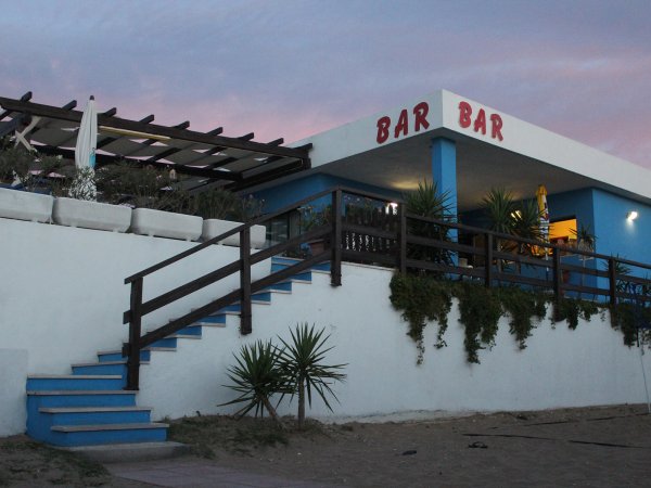 Un bar dipinto di bianco e blu con una terrazza in legno, cielo al tramonto sopra.
