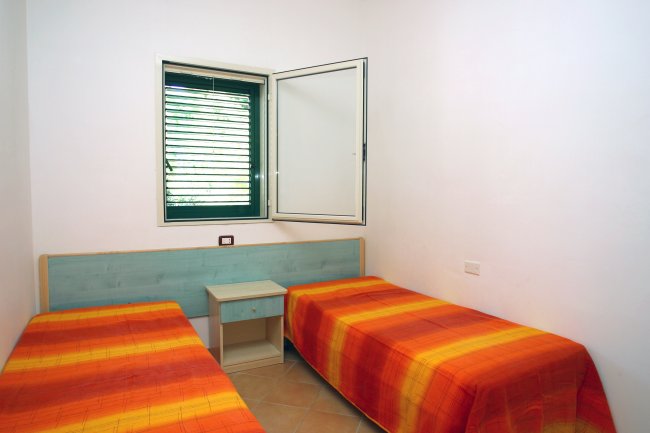 Camera con due letti singoli, coperte arancioni, una finestra e un comodino centrale.