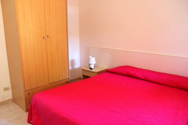 Camera da letto con copriletto rosso, armadio in legno e lampada su un comodino.