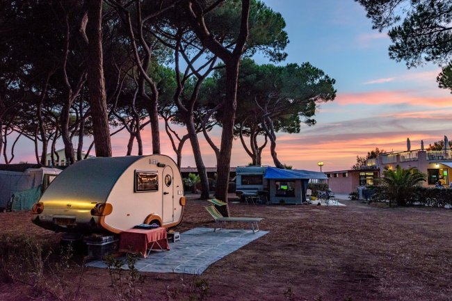 Una roulotte bianca in un campeggio tra gli alberi al tramonto.