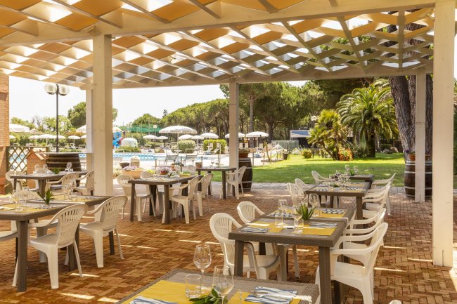 Ristorante all'aperto con tavoli apparecchiati, vista sulla piscina e giardino.