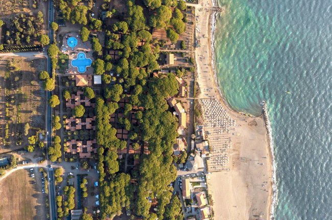Vista aerea di un villaggio turistico con piscine, pineta e spiaggia.