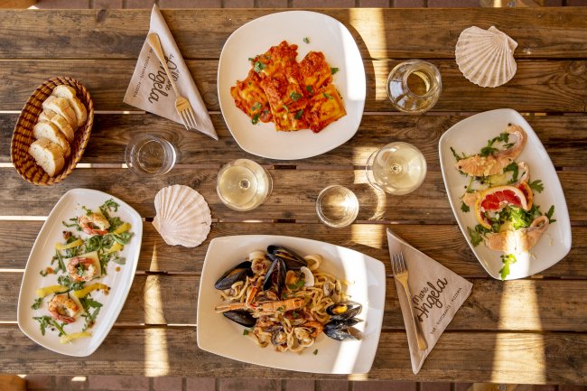 Tavolo di legno con piatti di pasta, pane e bicchieri di vino.