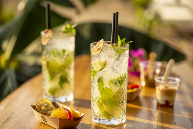 Due bicchieri di cocktail con lime e menta su un tavolo di legno, accanto a stuzzichini.