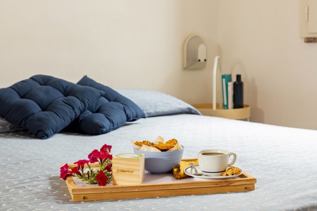Vassoio con colazione, fiori e caffè su un letto con cuscini blu.