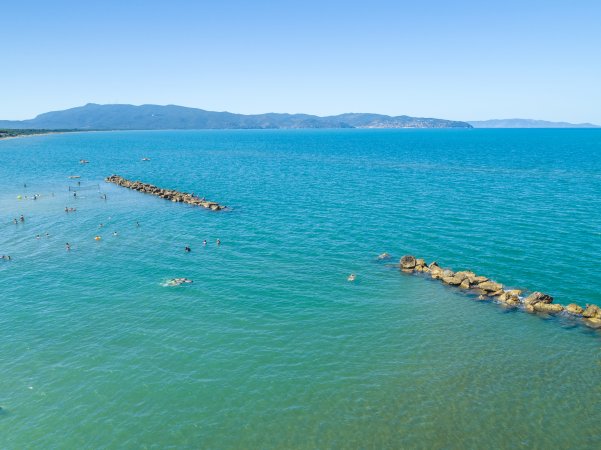 Vista panoramica del mare con scogliere e persone che nuotano.