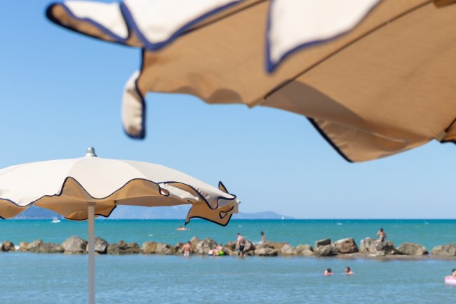 Due ombrelloni in primo piano con mare e bagnanti sullo sfondo.
