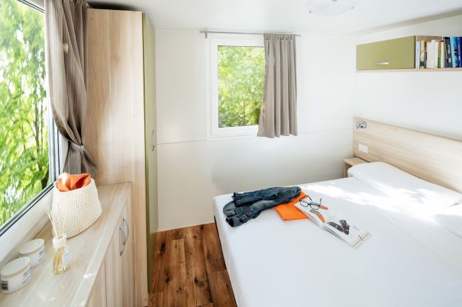 Camera da letto luminosa con letto matrimoniale, finestra e pavimento in legno.