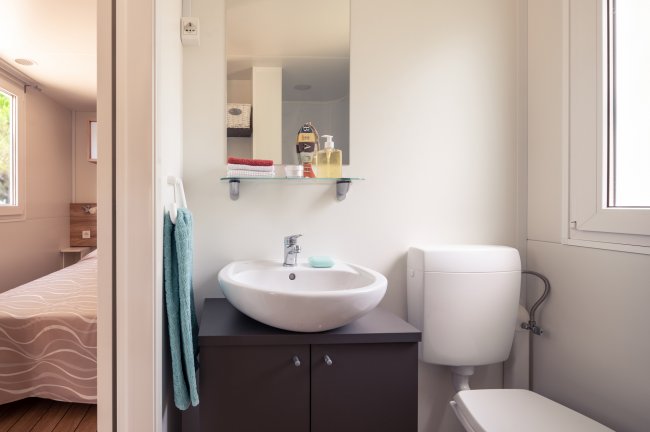 Bagno con lavabo moderno, specchio sopra, WC e asciugamano appeso.