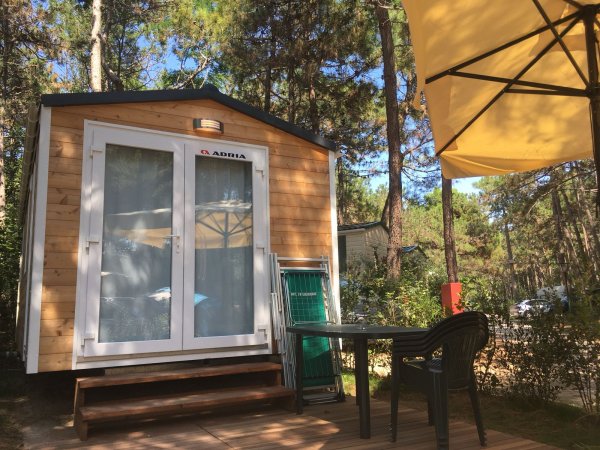 Una casetta in legno con veranda, ombrellone e sedia all'aperto.