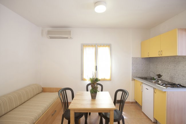 Cucina con tavolo e sedie, divano a destra, cucina gialla a sinistra.