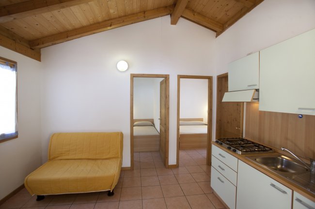 Interno con divano giallo, cucina e due porte alla camera da letto.