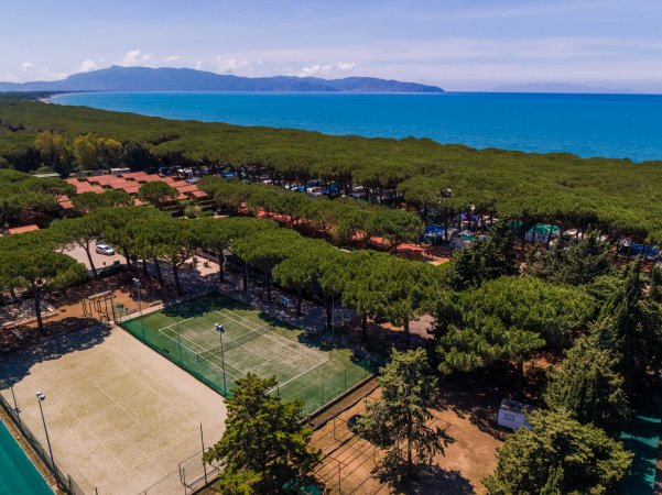 Campo da tennis tra alberi e vista sul mare con montagne lontane.