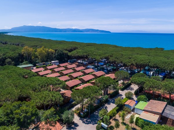 Villaggio con bungalow tra pini, mare turchese e montagne lontane.