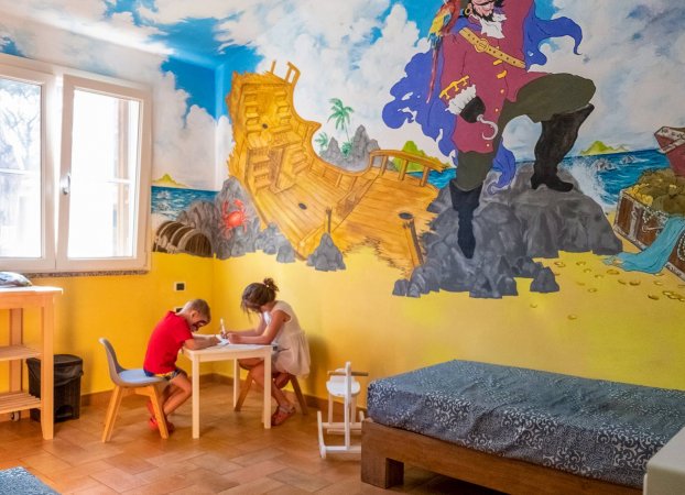 Due bambini disegnano in una stanza con murale di pirata e nave.