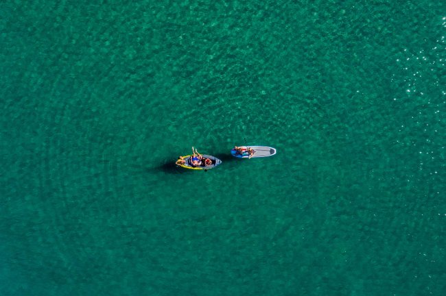 Due persone in un kayak e uno stand-up paddle in acqua turchese, viste dall'alto.