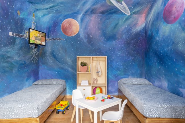 Stanza per bambini con pareti a tema spazio e due letti singoli.