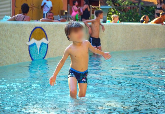 Un bambino sfocato gioca in una piscina poco profonda con persone sullo sfondo.