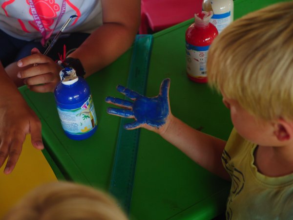 Bambino con la mano dipinta di blu osserva il colore. Sul tavolo ci sono bottiglie di vernice.