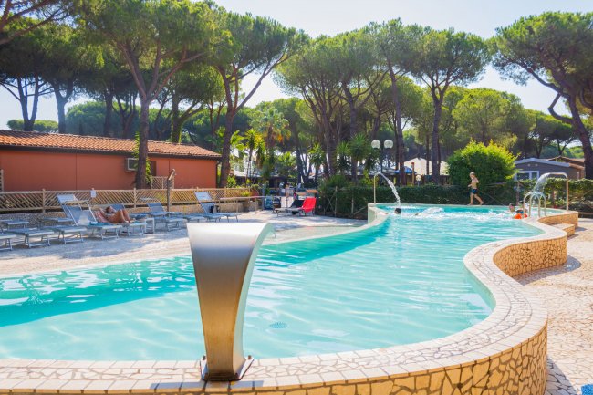Piscina con bordo in pietra, lettini a sinistra e alberi sullo sfondo.
