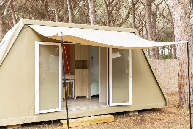 Una tenda moderna con apertura frontale in un bosco di pini.