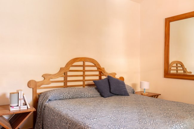 Una camera con letto matrimoniale, cuscini blu, comodini e un grande specchio con cornice in legno.