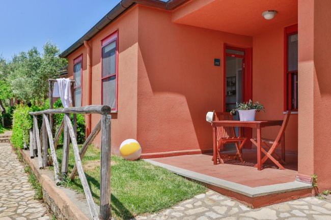 Entrata di una casa arancione con veranda, mobili da esterno e palla colorata sul prato.