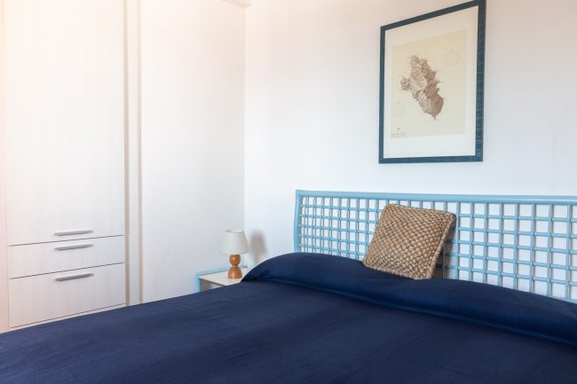 Una camera da letto con copriletto blu, quadro sulla parete e comodino con lampada.