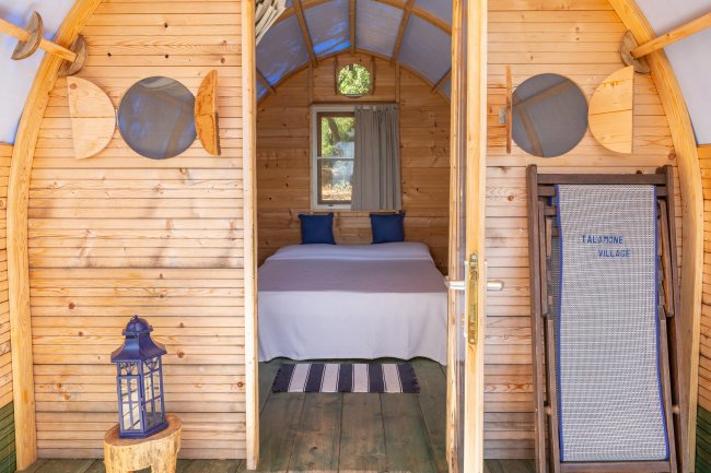 Interno di una cabina in legno con letto, lanterna blu e sedia a sdraio.