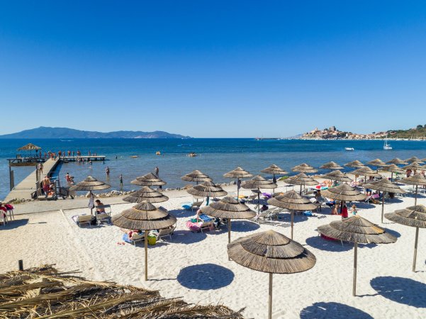 Spiaggia sabbiosa con ombrelloni e molo sullo sfondo.