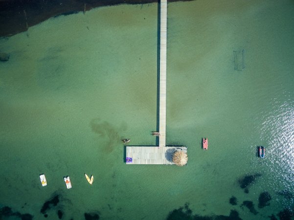 Vista aerea di un molo su acqua verde trasparente con pedalò colorati.