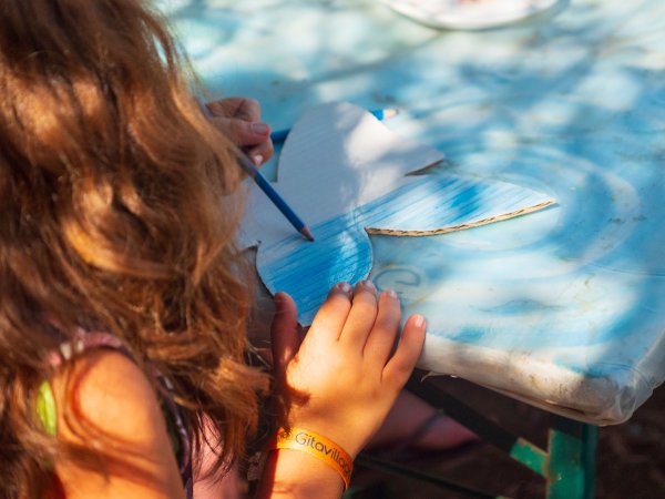 Bambina che colora un disegno a forma di farfalla blu su un tavolo soleggiato.
